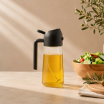 Black olive oil dispenser with olive oil next to a salad on a wooden table